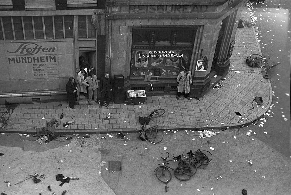 Abandoned bicycles, clothing and shoes on the corner of Dam Square and the Eggertstraat after the shooting of 7 May 1945; people take cover in doorways