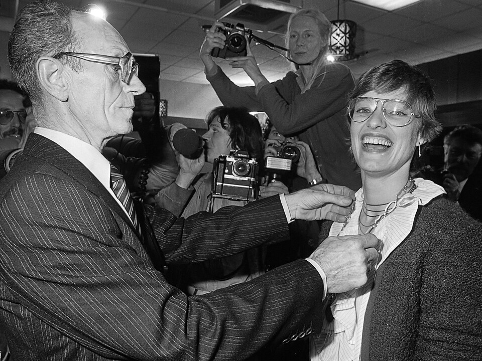 Party veteran Koert Stek (left) places the mayoral chain on a laughing Hanneke Jagersma, surrounded by photographers