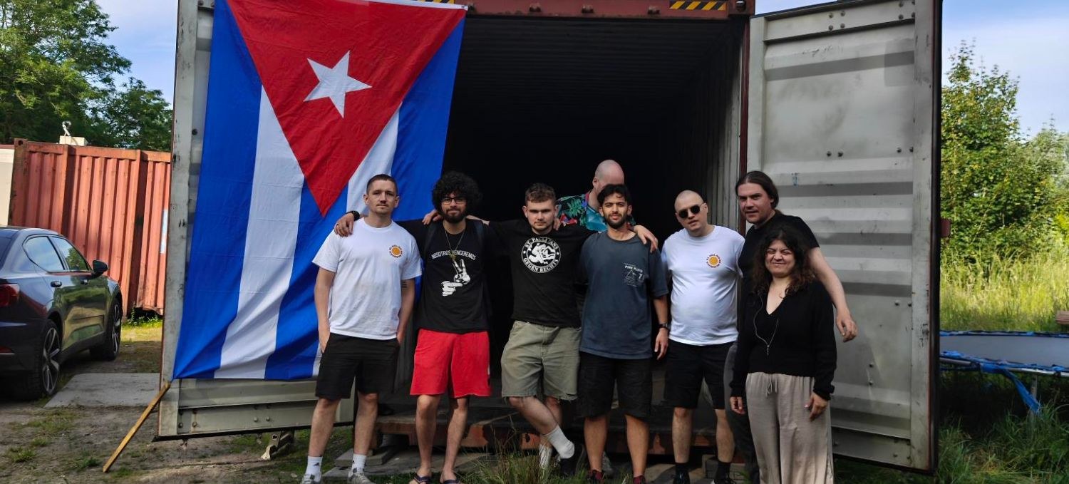 Een groep kameraden voor een geopende zeecontainer met een grote Cubaanse vlag en een rode CPN-vlag