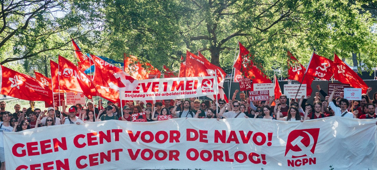 May Day demonstration with the banner "Not a cent for NATO! Not a cent for war!" and red flags
