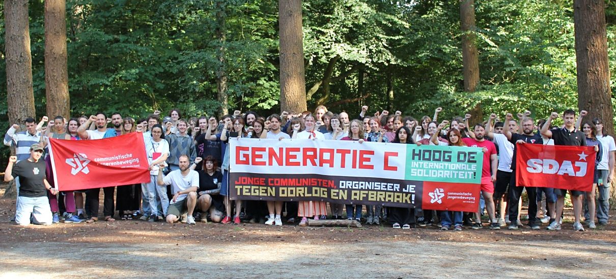 Group photo in the woods with raised fists and banners: "Generation C", "Long live international solidarity!" and the CJB