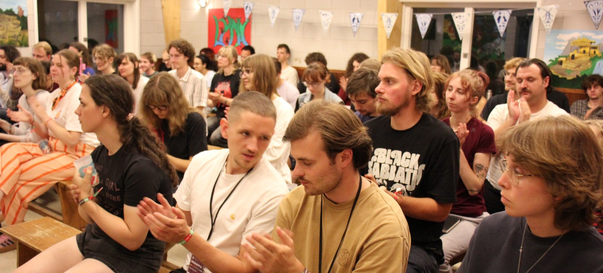A full hall of young people applauds during an education session at the CJB summer camp